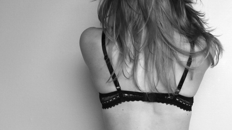 Schwarz-Weiß-Foto: Blick auf den Rücken einer Frau, die einen schwarzen BH trägt.