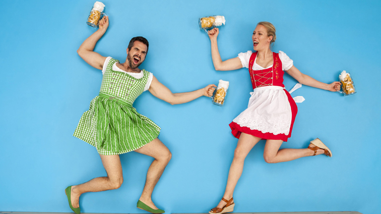 Mann und Frau in Dirndln tanzen mit Bierkrügen in den Händen