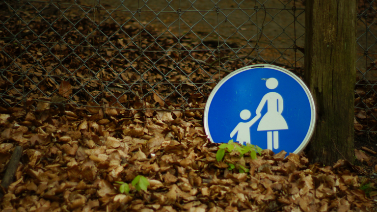 Ein "Mutter-und-Kind"-Straßenschild liegt im Laub.
