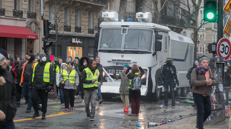 Ein Wasserverwerfer der Polizei, davor Demonstranten mit gelben Westen in den Straßen von Paris am 26.01.2019