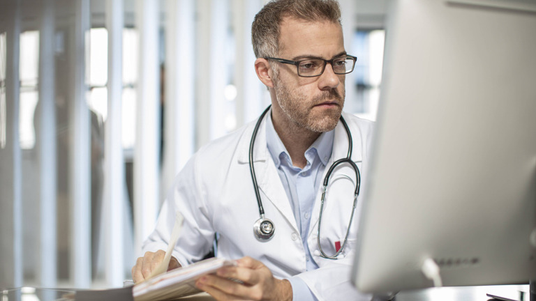 Arzt sitzt am Schreibtisch und schaut auf einen Computerbildschirm
