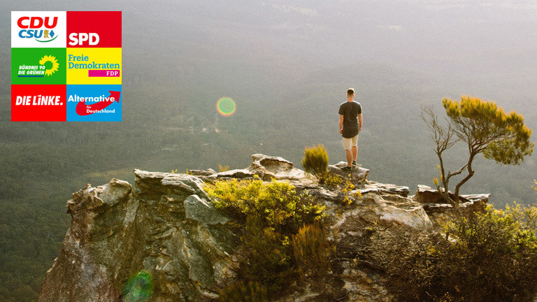 Ein Mann steht auf einem Felsen und blickt in die Ferne über einen Wald hinweg.