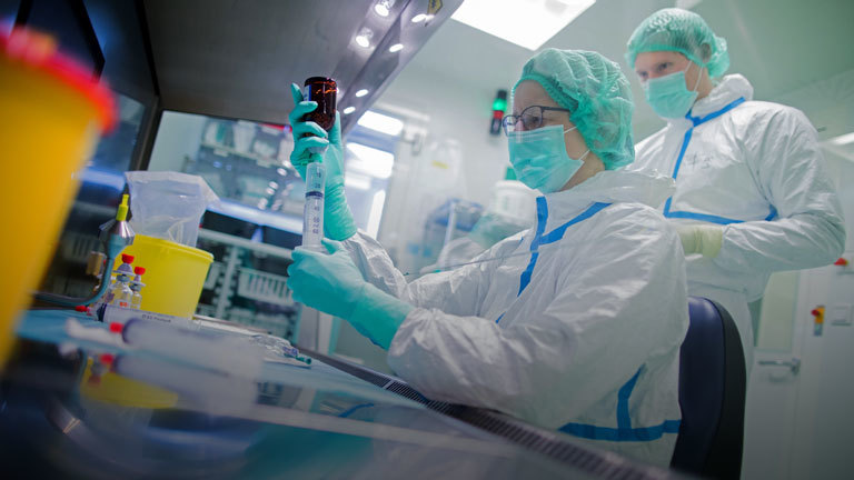 Zwei Mitarbeiter stellen in einem Reinraum Krebsmedikamente her.