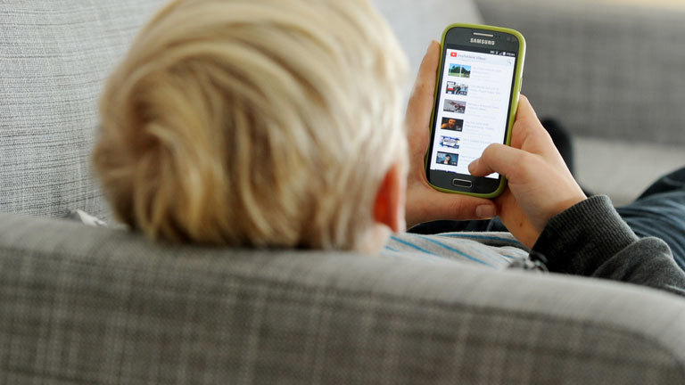 Ein Jugendlicher sitzt mit Smartphone auf einer Couch