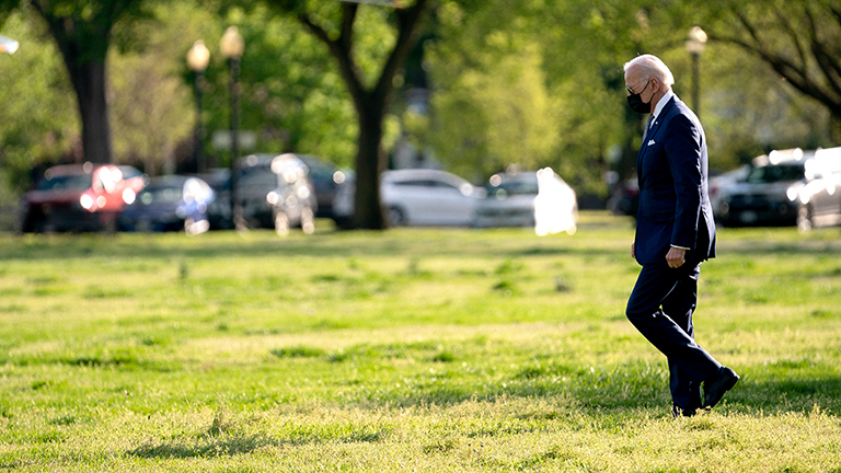US-Präsident Joe Biden geht über eine Wiese. Er trägt einen dunklen Anzug und eine Mund-Nase-Maske (16.04.2021)
