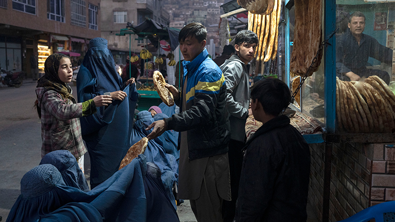 Vor einer Bäckerei in Kabul verteilt ein Mann Brot an Kinder und Frauen. Die Frauen tragen Burka. Sie strecken dem Mann die Hände entgegen. In Afghanistan herrscht Hunger; Foto: dpa (02.12.2021)