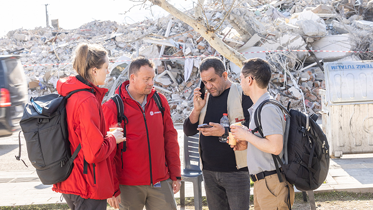 Vor einem zerstörten Gebäude stehen Janina Dreier von der Johanniter Unfallhilfe zusammen mit anderen Helfern. Sie ist in der Türkei nach dem schweren Erdbeben im Februar 2023.