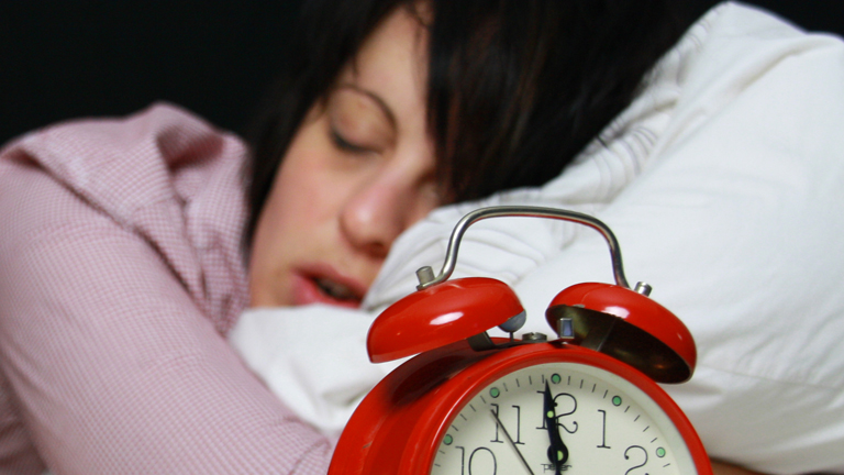 Eine Frau im Bett neben einem Wecker