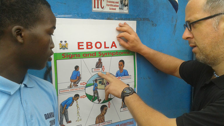 Zwei Männer stehen vor einer Ebola-Informationstafel.