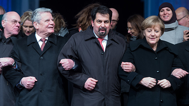 Bundestagspräsident Norbert Lammer (CDU - l-r), Bundespräsident Joachim Gauck, der Vorsitzende des Zentralrates der Muslime in Deutschland, Aiman Mazyek, und Bundeskanzlerin Angela Merkel (CDU) hacken sich am 13.01.2015 bei einer Mahnwache für die Opfer der Anschläge in Frankreich vor dem Brandenburger Tor in Berlin unter.