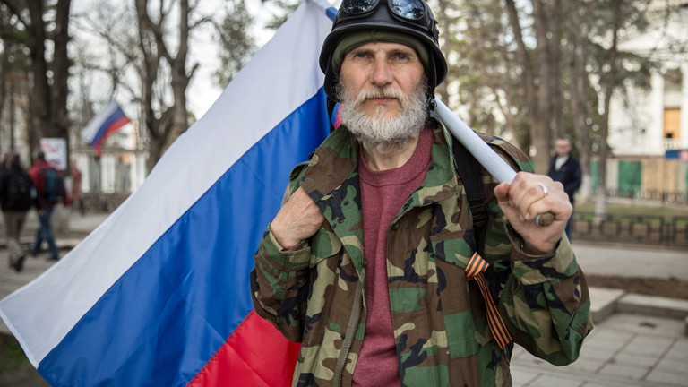 Ein älterer Mann mit der Fahne der Ukraine steht am 06.03.2014 vor dem Parlament in Simferopol, er trägt Helm und Militärjacke.