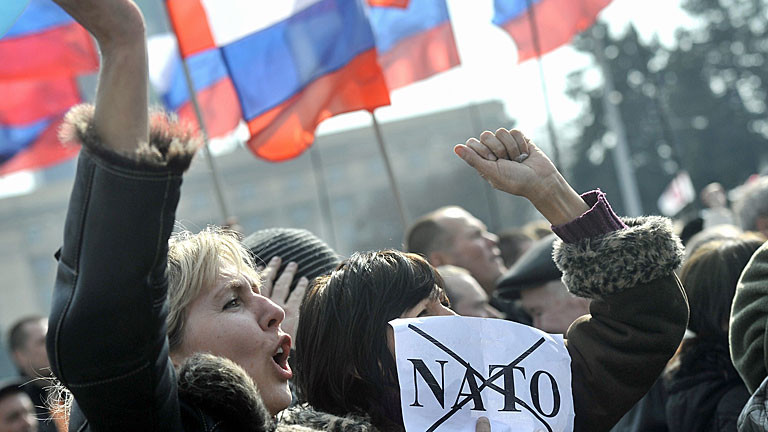 Bei einer Demo in Donetsk in der Ukraine hält eine Frau ein Schild mit dem durchgestrichenen NATO-Schriftzug hoch