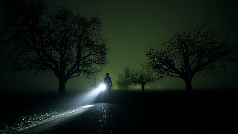 Eine Frau mit Taschenlampe leuchtet durch die Nacht