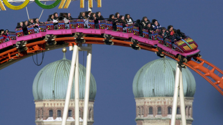 Vor der Kulisse der Münchner Frauentürme winkt ein Mann am Samstag (16.9.2000) aus dem Fahrgeschäft Olympia-Looping (dpa).