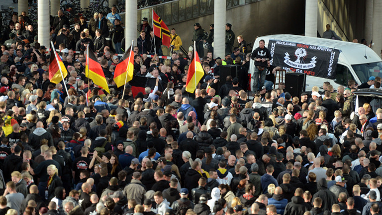Demonstranten stehen am 26.10.2014 in Köln (Nordrhein-Westfalen) vor einem Fahrzeug mit einem Transparent der als gewaltbereit bekannten Gruppe «Hooligans gegen Salafisten» (HoGeSa). (dpa)