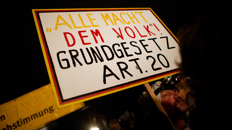Auf einer Pegida-Demo hält ein Demonstrant ein Schild: "Alle Macht dem Volk! Grundgesetz Art. 20"