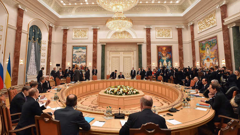 Kremlchef Wladimir Putin gestikuliert am 11.02.2015 im weißrussischen Minsk, während im Hintergrund Bundeskanzlerin Angela Merkel und der ukrainische Präsident Petro Poroschenko miteinander sprechen.