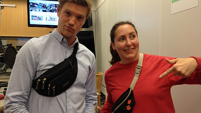 Thilo und Tina stehen im Studio und tragen beide Bauchtaschen.