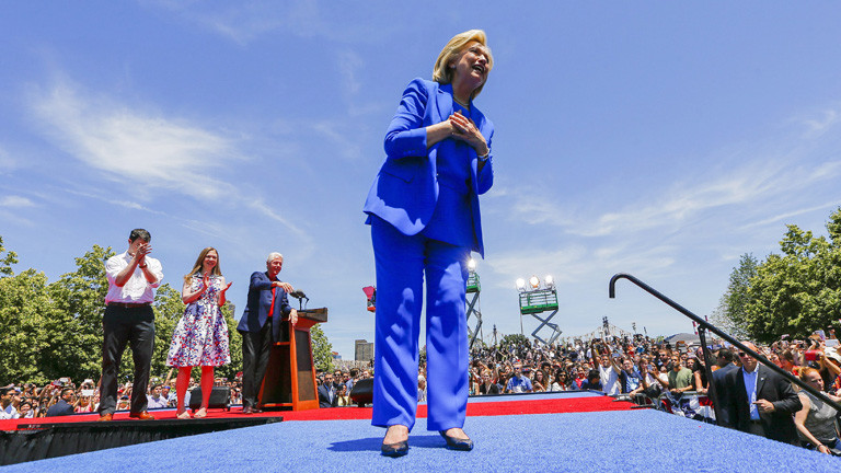 Hillary Clinton im blauen Hosenanzug auf einer Bühne. Sie hält ihre erste Wahlkampfrede; Bild: dpa