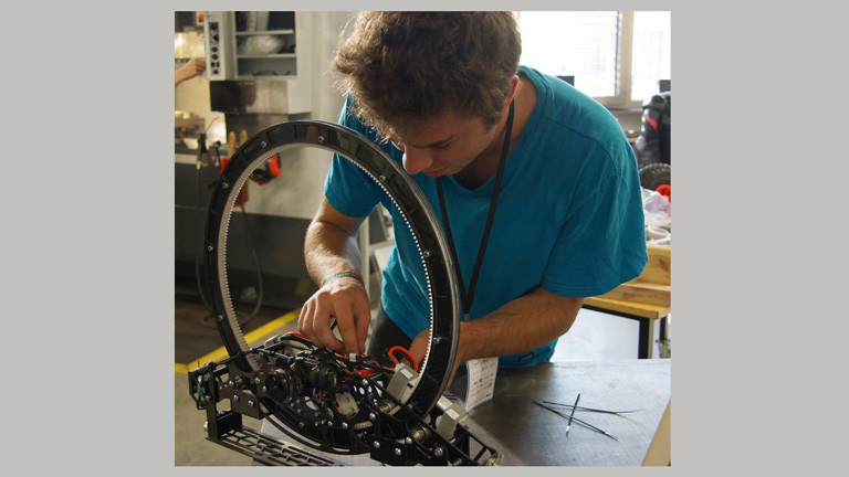 Maximilian Reif beugt sich über den Roboter für den Weltraumlift. Er fixiert Kabel.