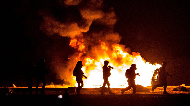 Bei der Räumung des Lagers in Calais. In der Nacht gehen Polizisten vor Feuern entlang.