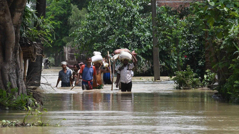 Nach schweren Regenfällen sind Regionen im indischen Bundesstaat Bihar unter Wasser. Menschen laufen durch Wasser und tragen Säcke auf den Köpfen.