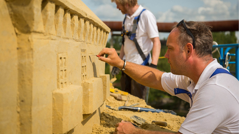 Ein Mann arbeitet an der fast fertigen Sandburg. Er arbeitet kleine Fenster in den Sand.