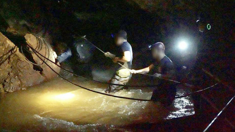 Rettungskräfte auf dem Weg zur Höhle, in denen ein Fußballteam und der Trainer gefangen sind. Die Retter stapfen durch tiefes Wasser.