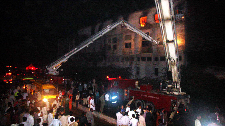 Am 11.09.2012 brennt eine Textilfabrik im pakistanischen Karatschi. Feuerwehrfahrzeuge stehen vor dem Gebäude. Rettungskräne sind ausgefahren. Hinter den Fenstern sieht man die Flammen.. Bei dem Brand starben 250 Menschen.