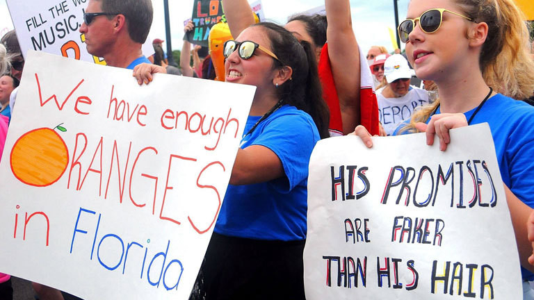 Demonstranten in Florida halten Schilder hoch. Sie protestieren gegen die erneute Kandidatur Donald Trumps für das Präsidentenamt.