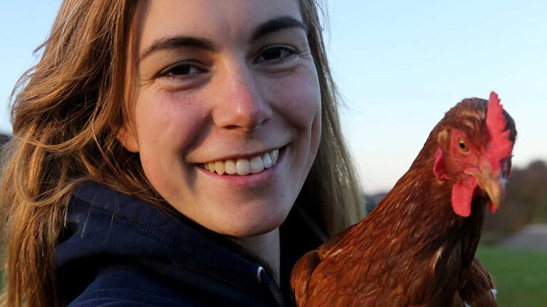 Portraitfoto von Marie Tigges, sie hält ein Huhn auf dem Arm.