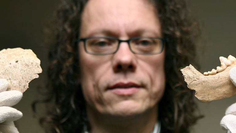 Der Archäologe Jörg Orschiedt zeigt den Teil eines menschlichen Schädels (l) und einen Wolfskiefer