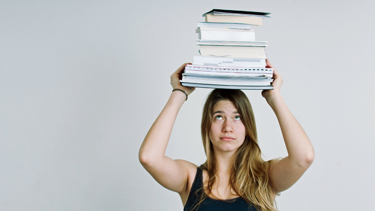 Eine junge Frau trägt Bücher und Unterlagen auf dem Kopf.