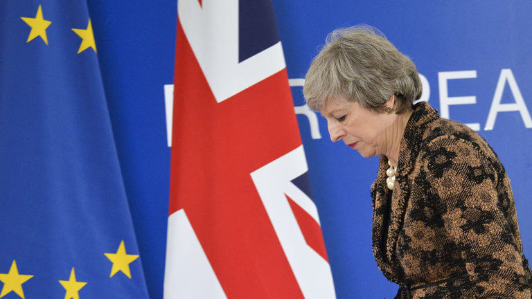 Theresa May blickt deprimiert und läuft an der britischen und europäischen Flagge vorbei