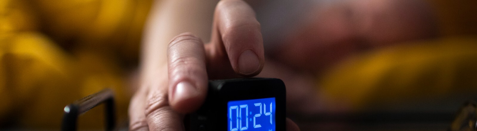 Mann liegt im Bett und schaltet seinen Wecker ein.