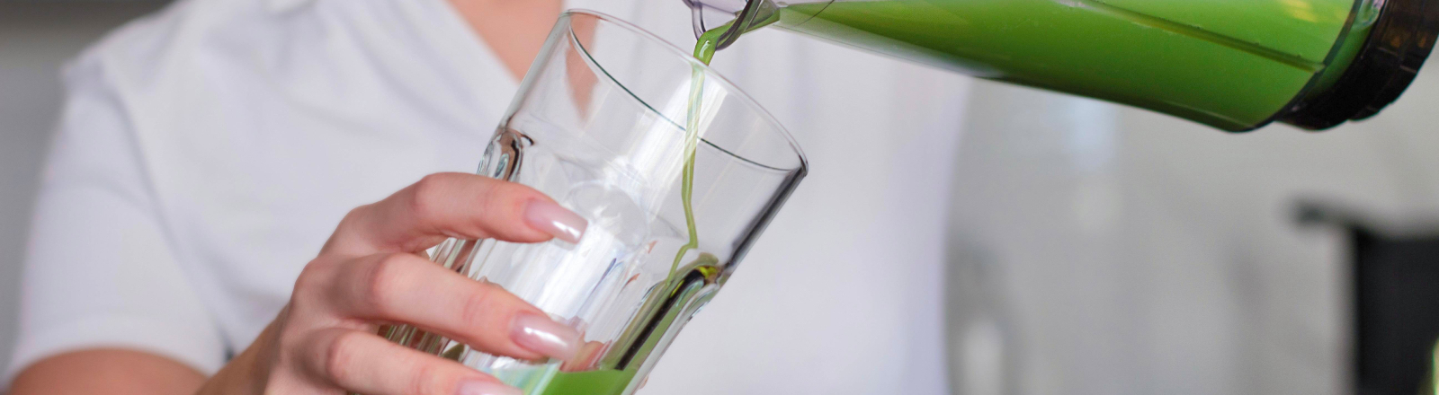Eine Frau in einem weißen T-Shirt gießt einen grünen Smoothie in ein Glas.