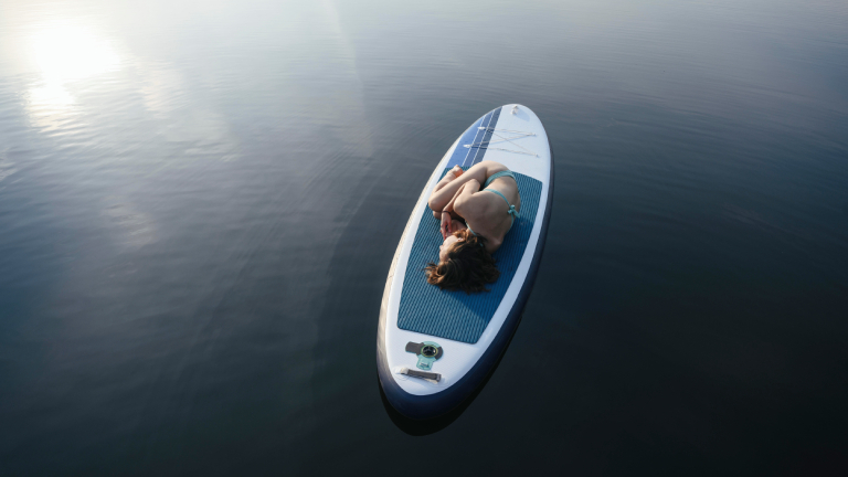 Eine Frau liegt gekrümmt auf einem Surfbrett, das auf dem Wasser schwimmt.