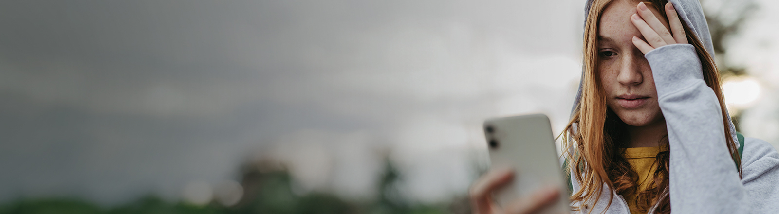 Foto einer jungen Frau, die traurig auf ihr Smartphone guckt und die Hand an die Stirn legt.
