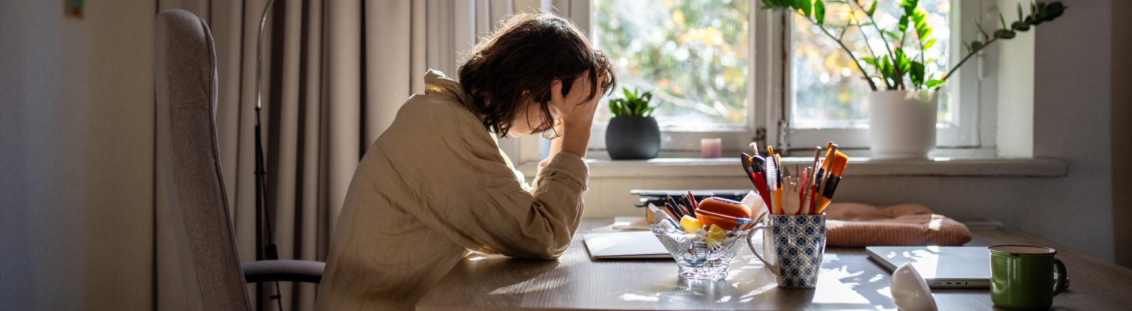 Eine offensichtlich verschlafene, halbwache Frau sitzt an einem Tisch und stützt den Kopf auf ihre rechte Hand