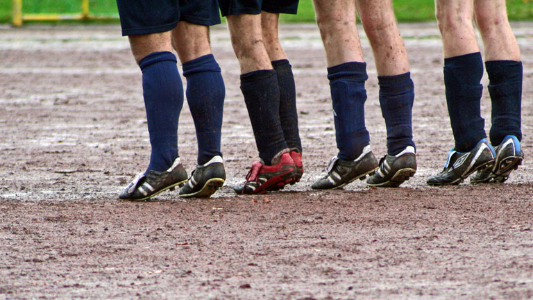 Fußballer, die im Matsch auf ihren Zehenspitzen stehen.