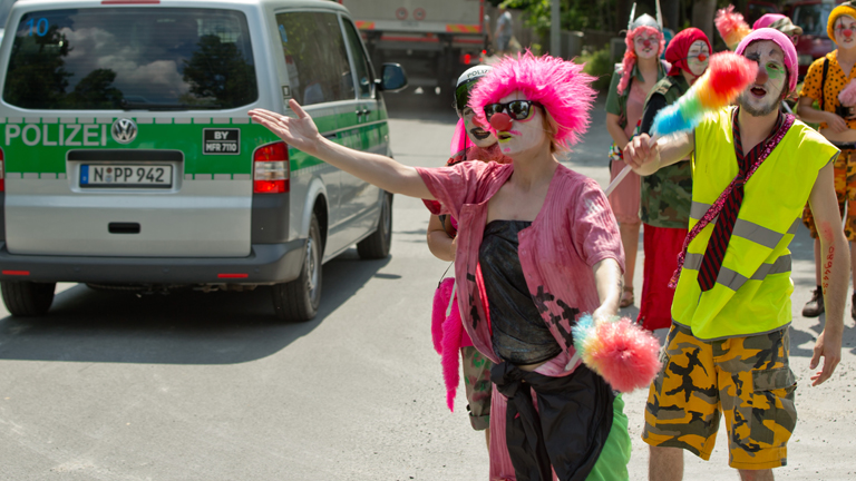 Als Clowns verkleidete Demonstranten winken am 05.06.2015 in Garmisch-Partenkirchen (Bayern) am Rande einer Demonstration gegen den G7-Gipfel zu vorbeifahrenden Polizeifahrzeugen.