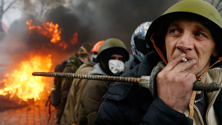 Demonstranten in Kiew haben sich am 20.02.2014 zu einer Verteidigungslinie formiert. Sie tragen Helme, einer von ihnen raucht. Auf der Straße brennt Gerümpel.
