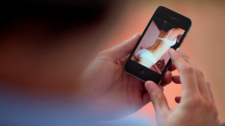 Ein Mann schaut sich auf einem Handy eine junge Frau in Unterwäsche an.