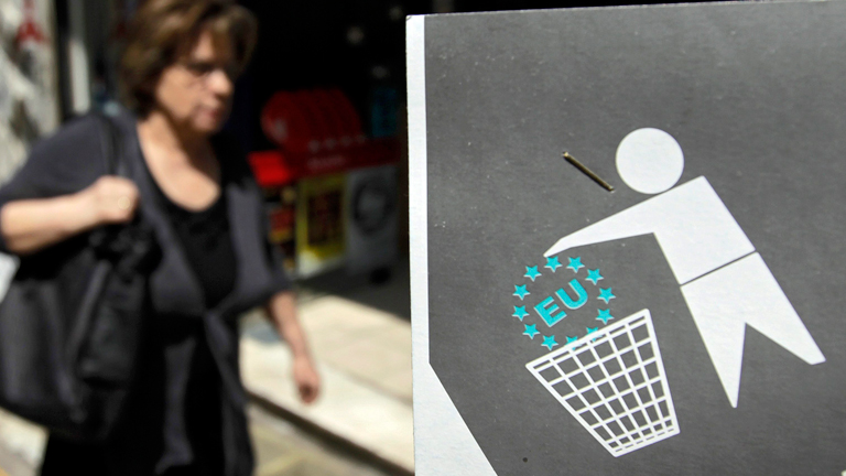 Eine Griechin geht an einem Plakat vorbei, auf dem Der Euro in den Müll geworfen wird.