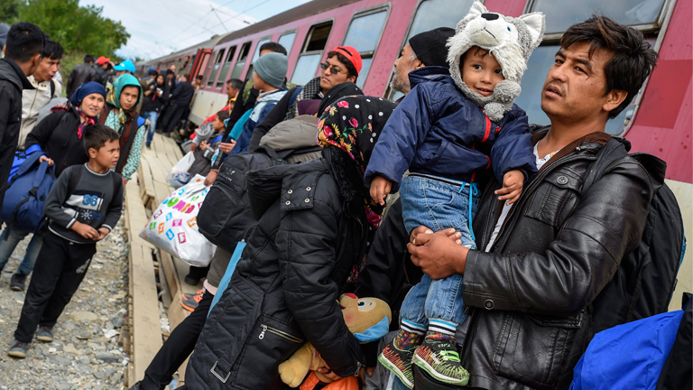 Flüchtlinge stehen vor einer Bahn.