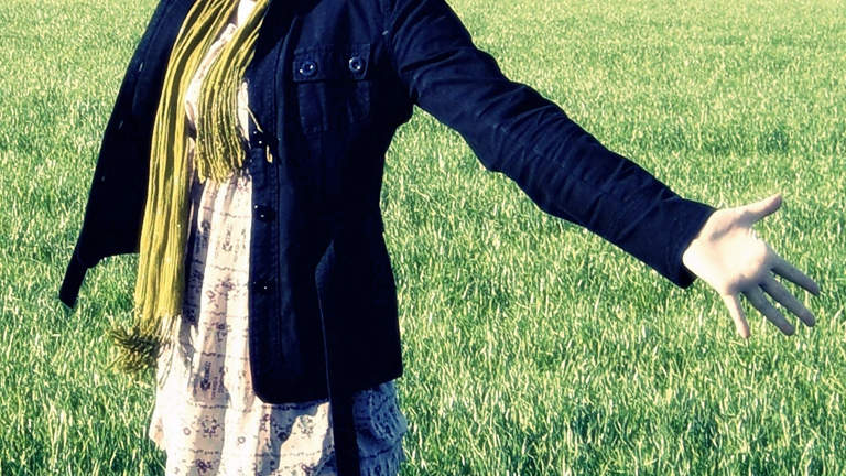 Eine Frau steht auf einer Wiese und streckt den Arm aus.