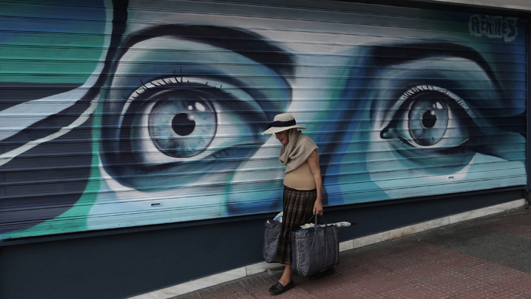 Eine Frau geht an einem geschlossenen Geschäft in Griechenland vorbei.