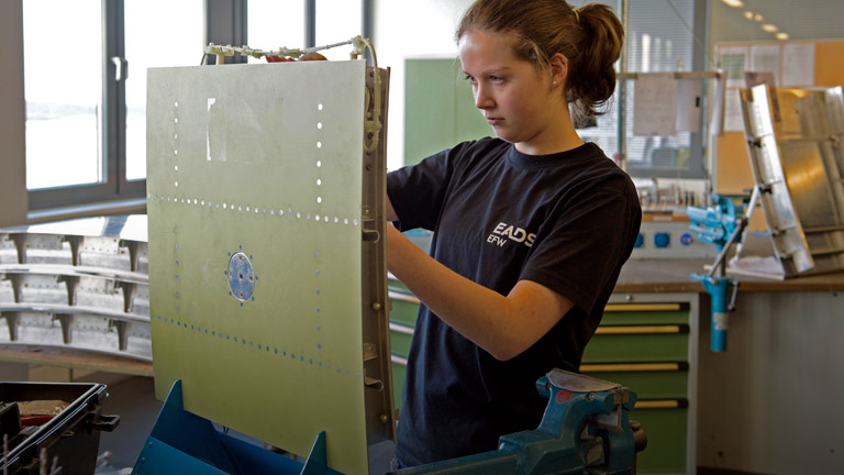 Eine junge Auszubildende arbeitet beim Unternehmen EADS an einem Flügelteil.