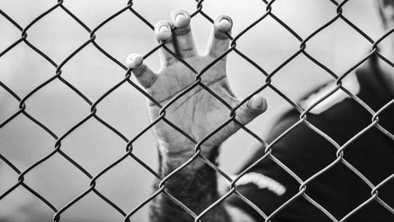 Eine Hand krallt sich in einen Zaun.