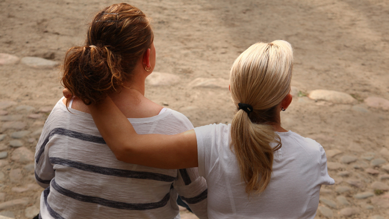 Zwei Frauen sitzen am 08.09.2013 in Berlin auf einer Bank. Die eine legt den Arm um die andere.